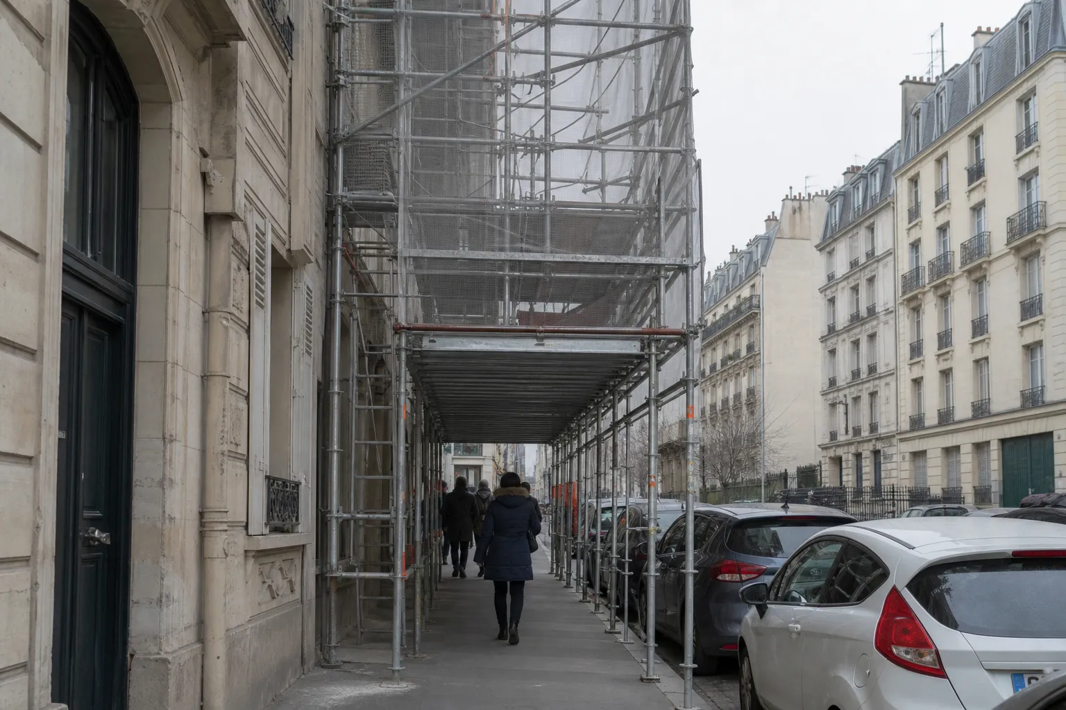 Échafaudage monté au-dessus d’un trottoir parisien étroit, tunnel piéton au rez-de-chaussée et filet sur les étages