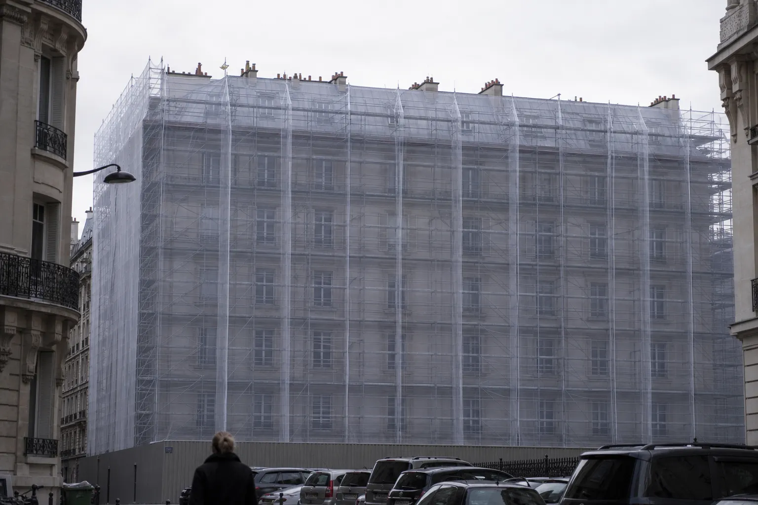 Immeuble parisien entièrement bâché et échafaudé pour une campagne de toiture, vu depuis la rue
