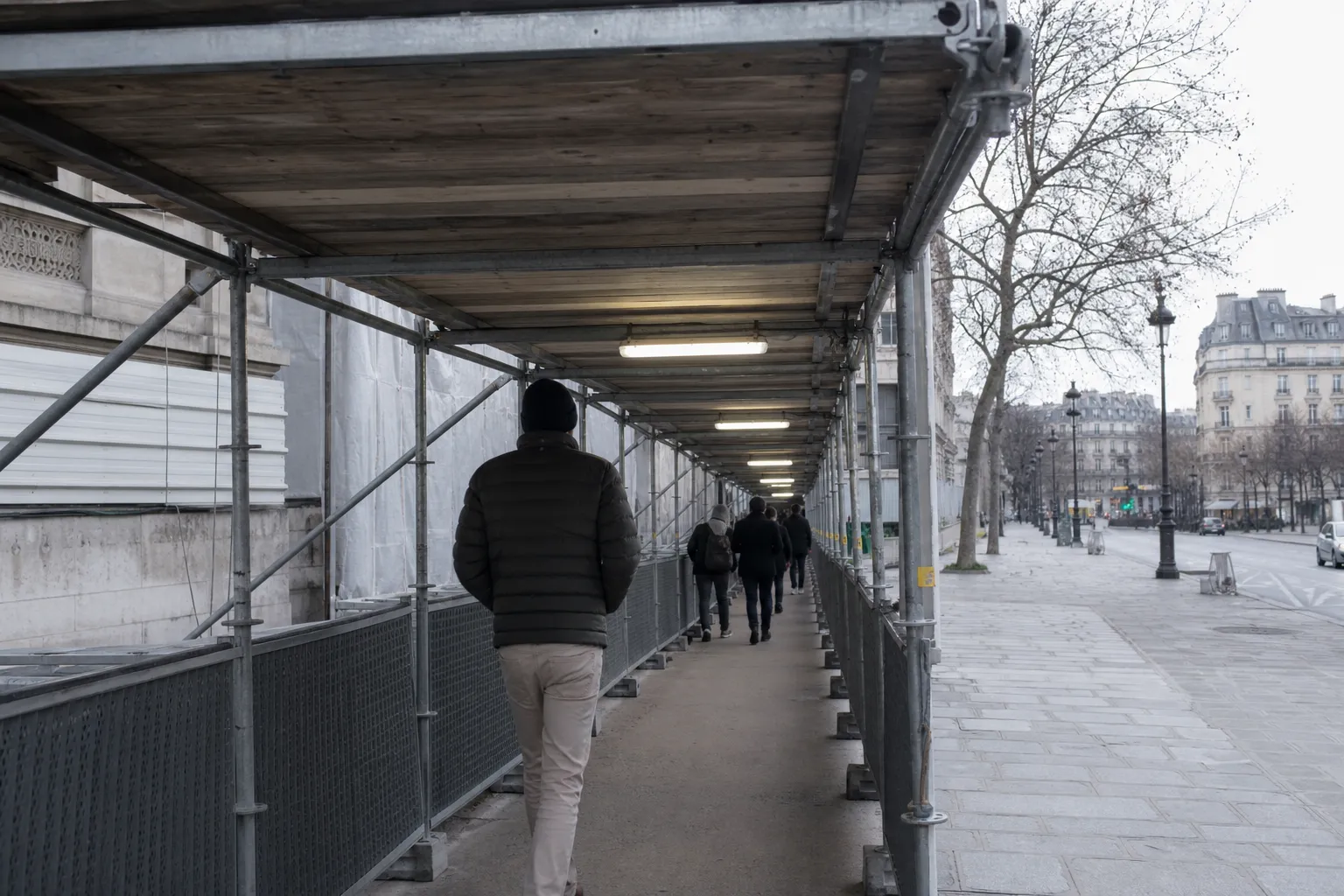Tunnel piéton sous un échafaudage de trottoir parisien, platelage bois au-dessus et cheminement éclairé