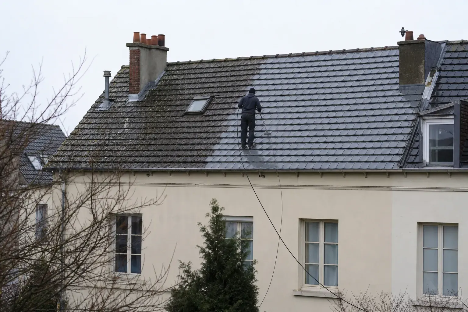 Lance de nettoyage basse pression posée sur un toit de tuiles moussues, tuyau descendant vers le sol