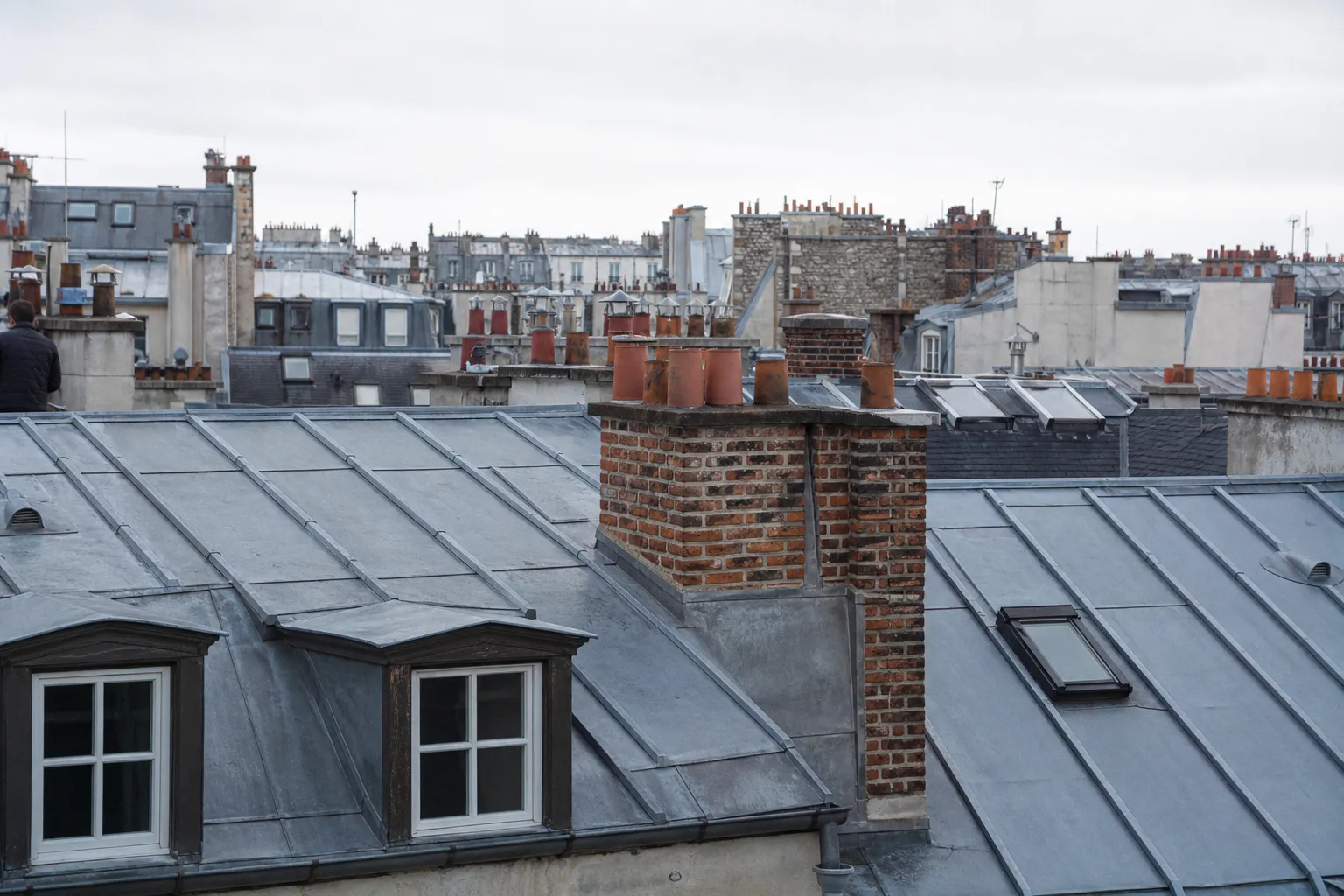Nappe de toits de zinc parisiens vue de près, joints debout parallèles et souches de cheminée en brique