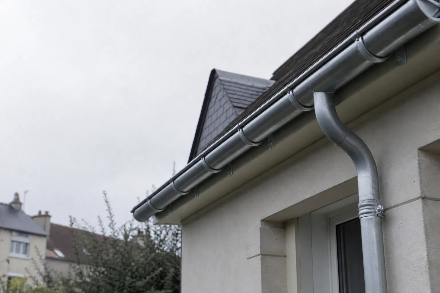 Gouttière demi-ronde en zinc neuve fixée à l’égout d’un pavillon, crochets et col de cygne de descente
